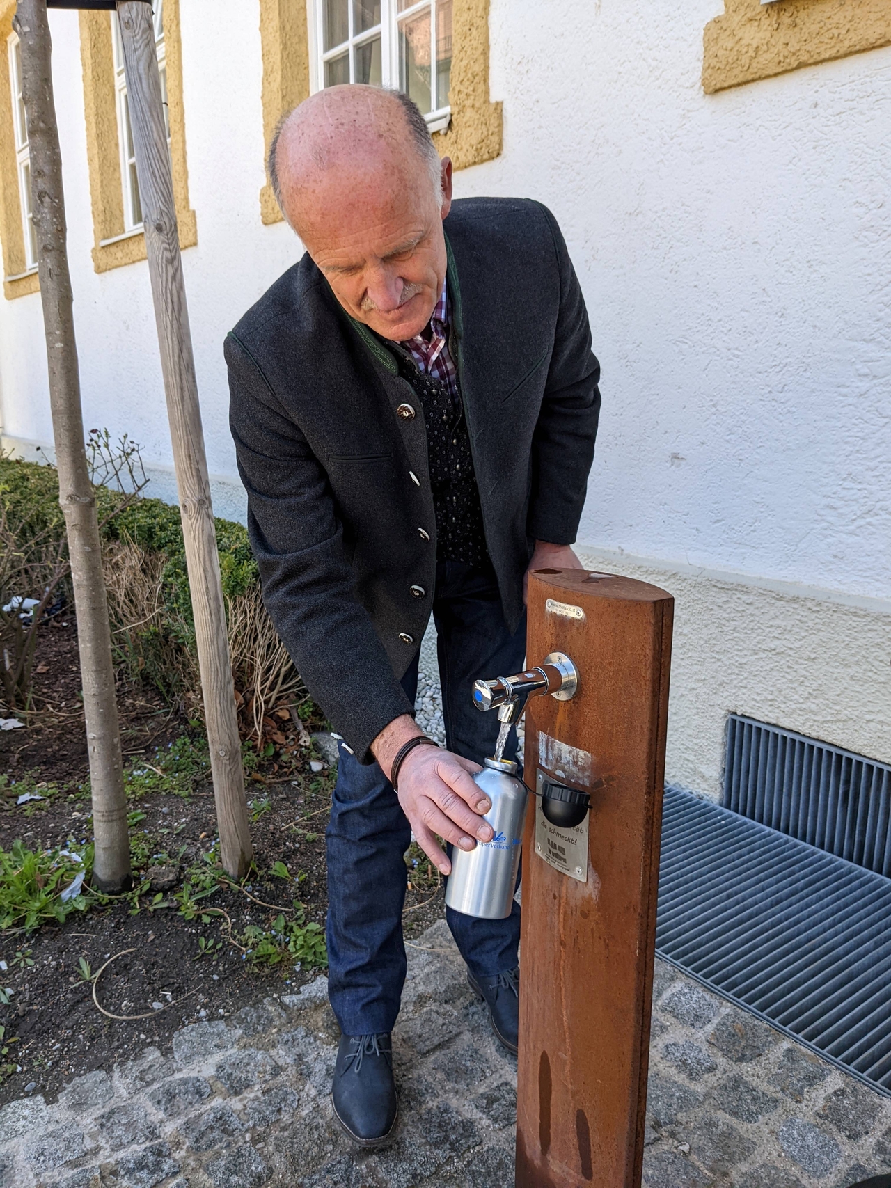 Eine Person füllt eine Wasserflasche am Trinkbrunnen neben der Alten Schule in Gröbenzell auf