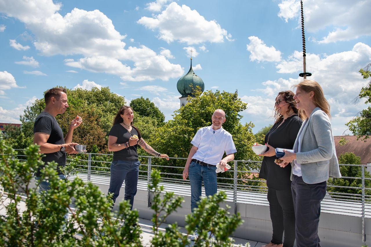 Mitarbeitende der Gemeinde Gröbenzell stehen in der Mittagspause im Halbkreis auf der Dachterrasse des Rathauses und unterhalten sich