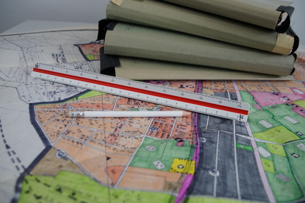 Ein Lineal, Bleistift und Mappen mit Unterlagen liegen zusammen auf einem Flurplan