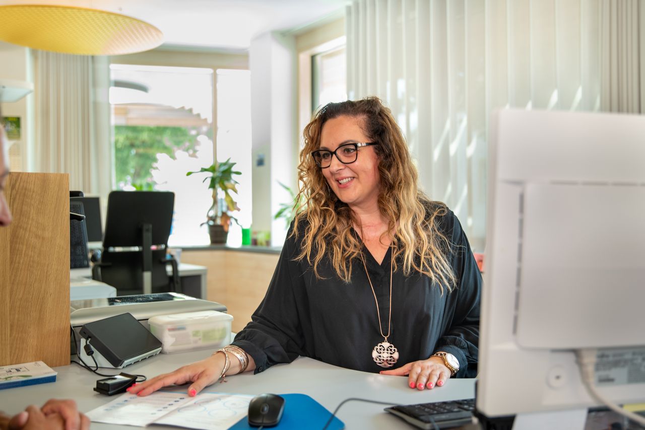 Eine Mitarbeiterin des Bürgerservices sitzt an ihrem Schreibtisch und spricht mit einem Bürger