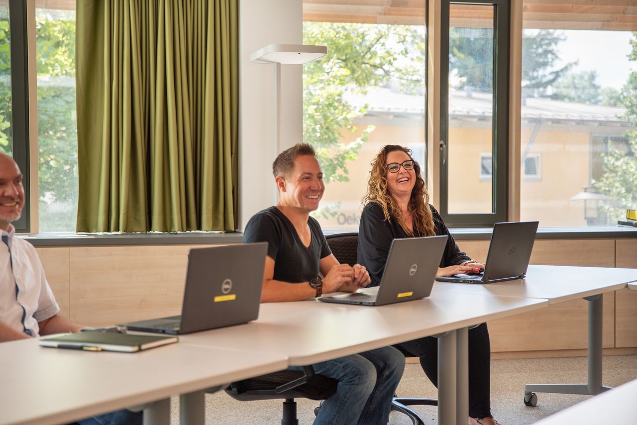 Schulungssituation: Gut gelaunte Mitarbeitende sitzen vor Laptops im Sitzungsraum