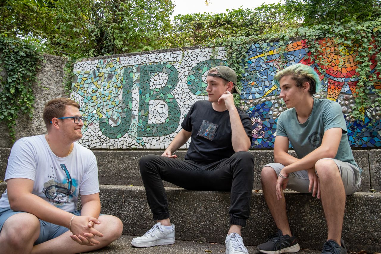 Jugendsozialarbeiter führt Gespräch mit zwei Jugendlichen auf einer Bank im Freien