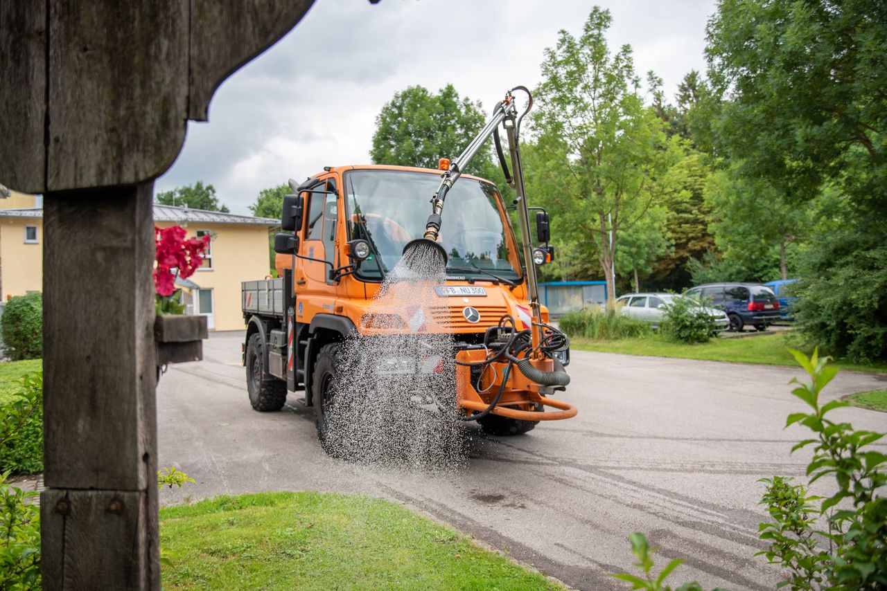 Gießfahrzeug der Gemeinde Gröbenzell gießt ein Blumenbeet.