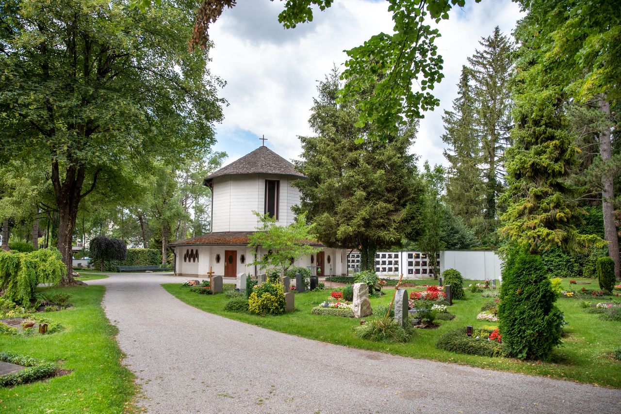 Die Aussegnungshalle am Gröbenzeller Friedhof, umgeben von Gräbern und Bäumen.