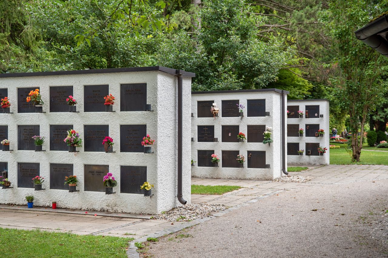 Mehrere weiße Wände mit Urnengräbern und Blumen am Gröbenzeller Friedhof