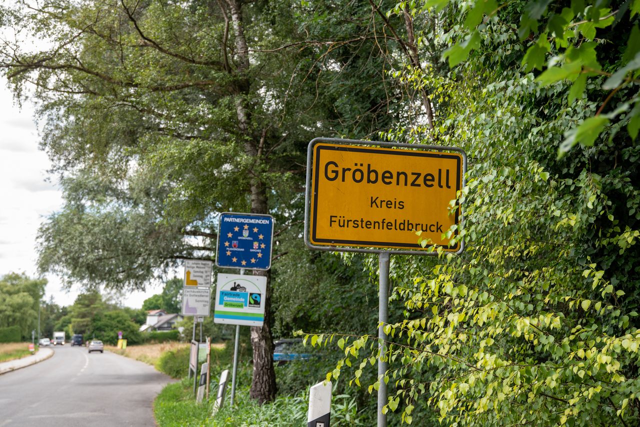 Ortsschild der Gemeinde Gröbenzell. Im Hintergrund ein Schild mit den Wappen der Partnergemeinde und eines für Gröbenzell als Fairtrade Kommune.