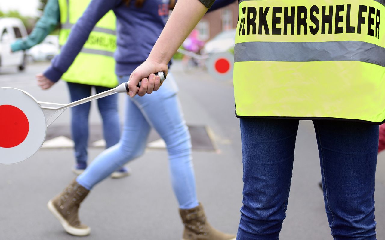 Schulweghelfer blockieren den Verkehr und helfen Kindern über die Straße