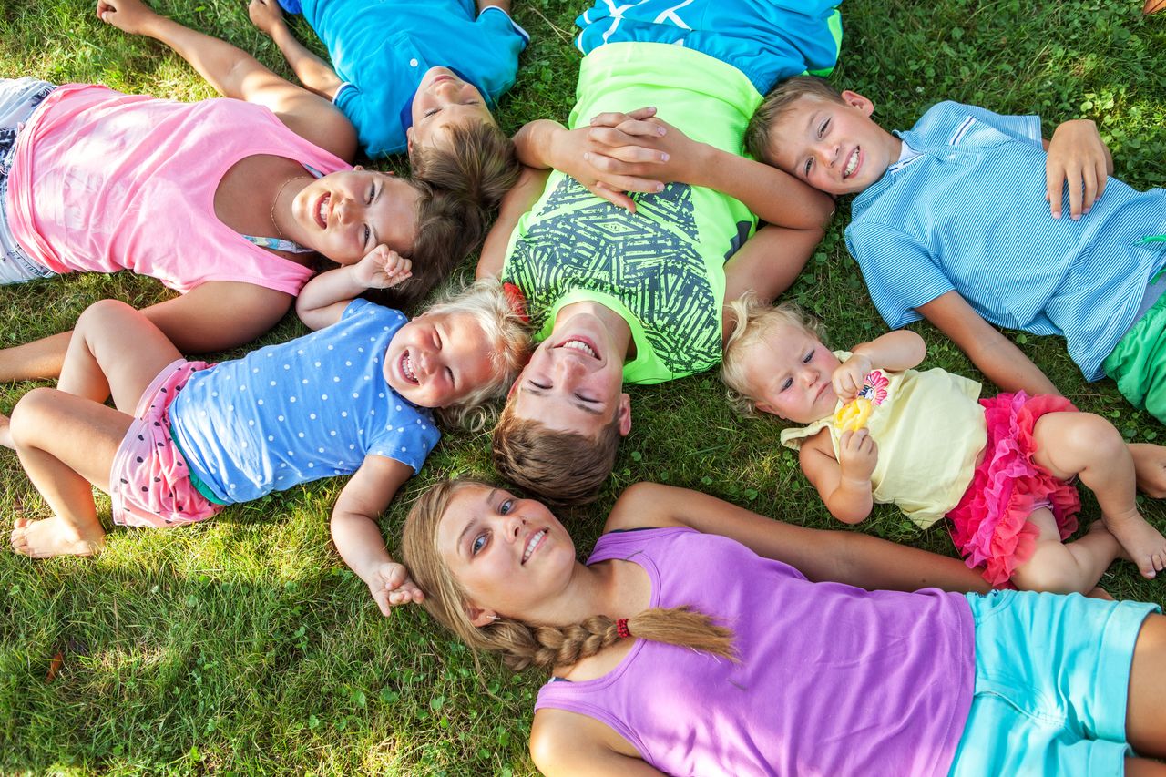 Kinder allen Alters liegen im Kreis im Gras