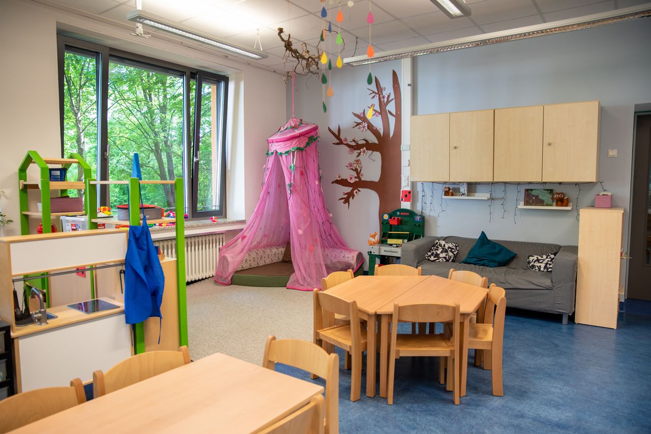 Ein Gruppenraum im Kindergarten Ährenfeldfüchse mit Gruppentischen und Stühlen sowie einer Couch und Kuschelecke mit rosa Baldachin