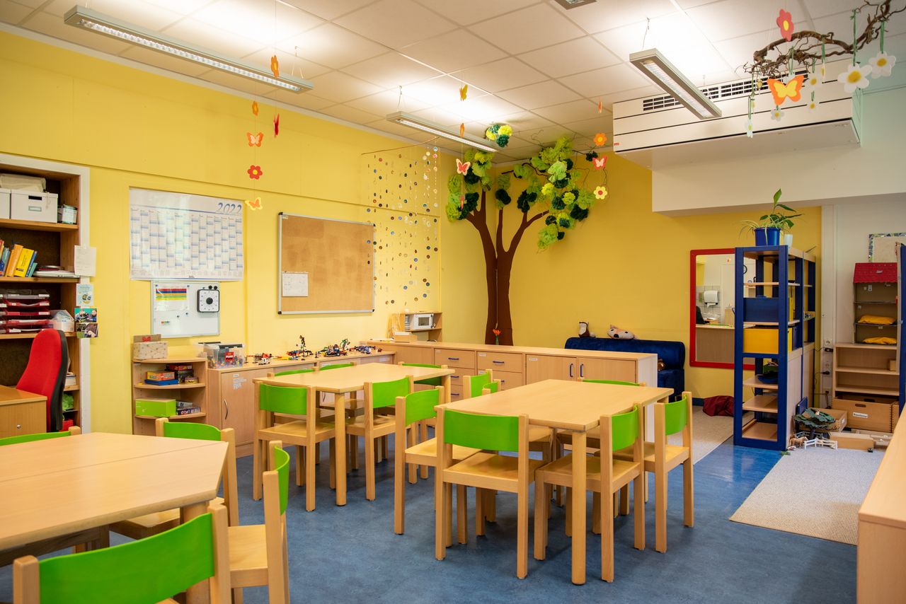 Ein Gruppenraum im Kindergarten Ährenfeldfüchse mit Gruppentischen und Stühlen, im Hintergrund eine Spielecke