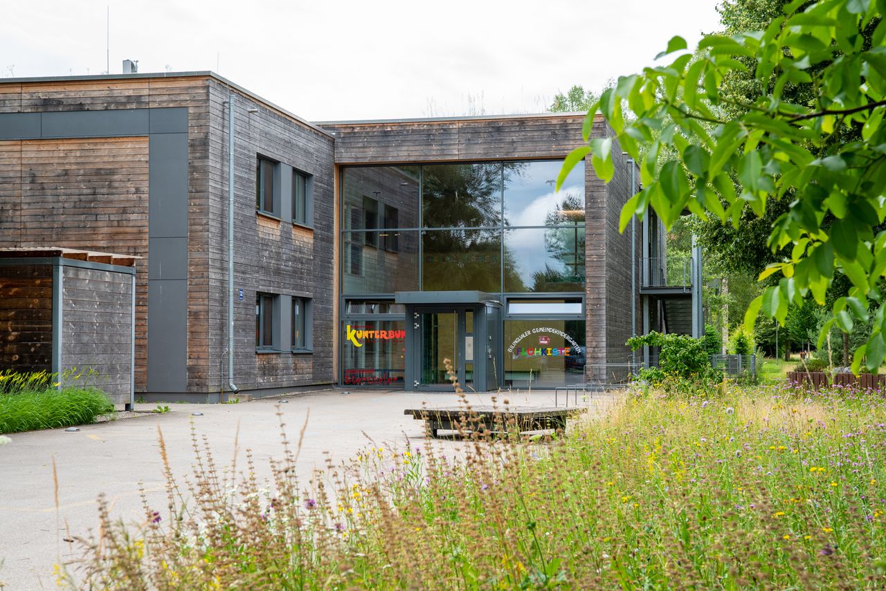 Außenansichten des Eingangs zum Kindergarten Flohkiste, rechts ein Streifen mit hohem Gras