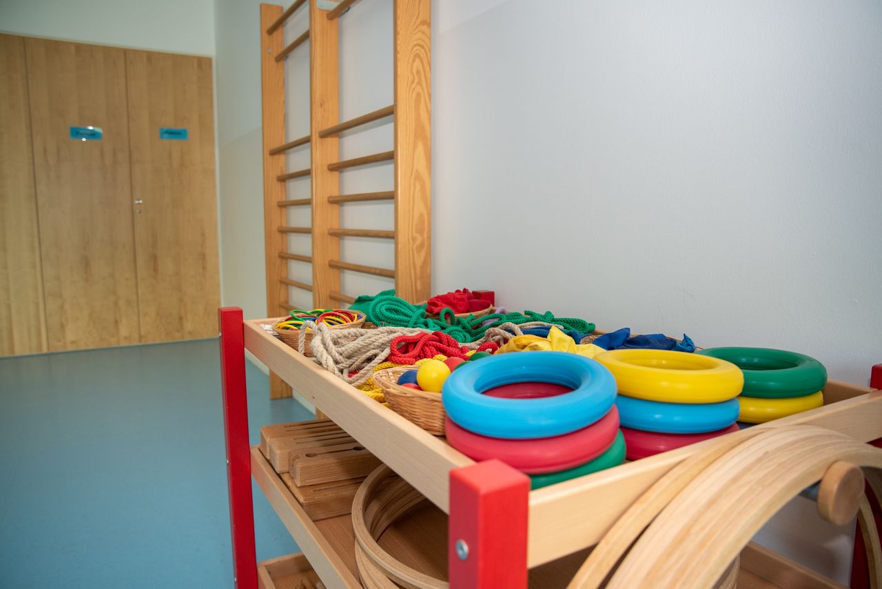 Turnraum im Kindergarten Flohkiste mit einer Sprossenwand, im Hintergrund Schränken und im Vordergrund einem Wagen mit Seilen, Ringen sowie Reifen