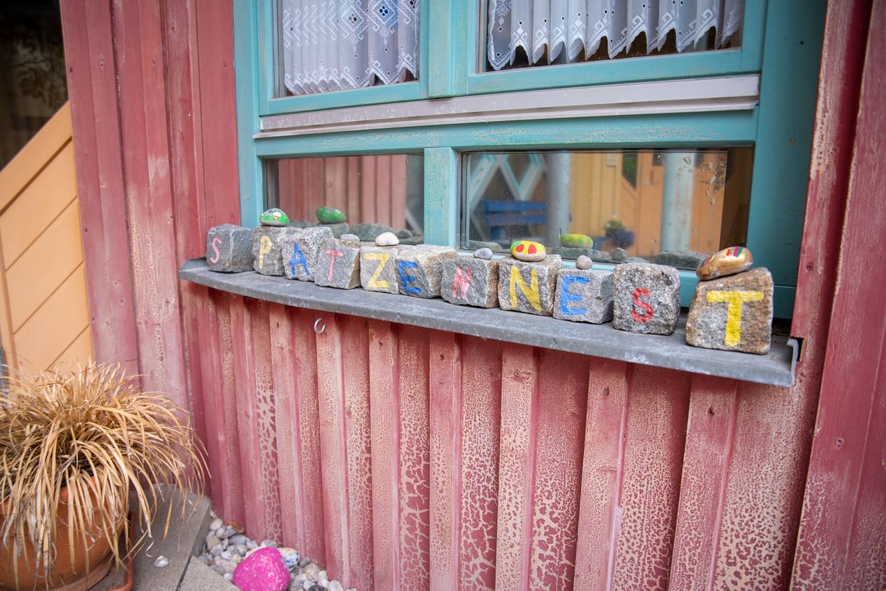 Aufgereihte Steine auf einem Fensterbrett im Eingangsbereich des Kindergartens Spatzennest, auf denen je einem Buchstaben steht. Zusammen ergeben sie den Namen des Kindergartens