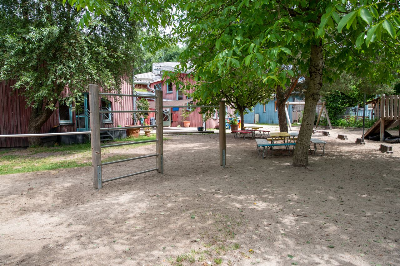 Garten des Kindergartens Spatzennest mit Reck- und Kletterstangen, einer Terrasse sowie Sitzgruppen unter Bäumen