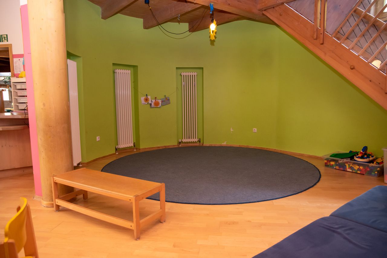 Ecke für Sitzkreis mit einer Sitzbank und einem Teppich, im Hintergrund Spielzeug