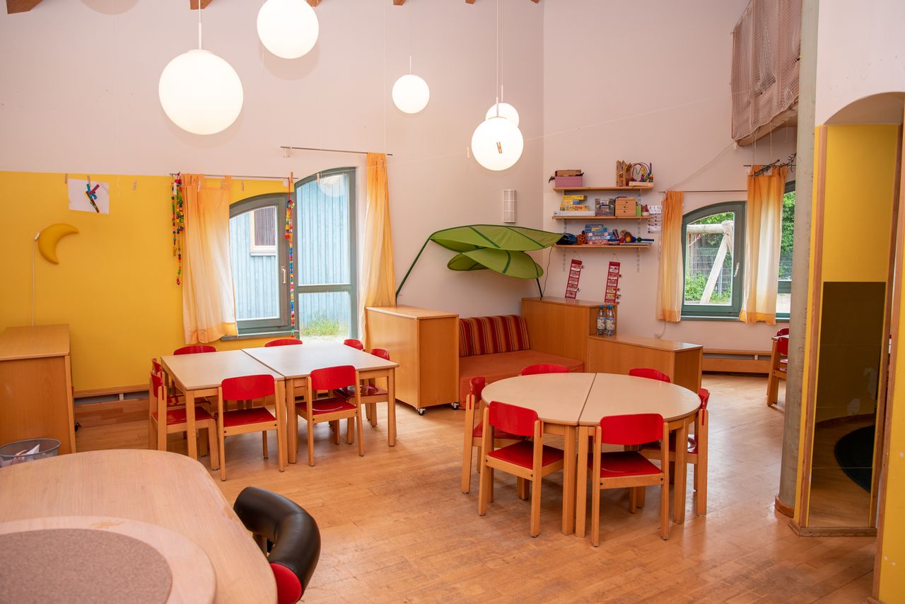 Gruppenraum mit Tischen, Stühlen und Regalen sowie einer Kuschelecke mit einer kleinen Couch