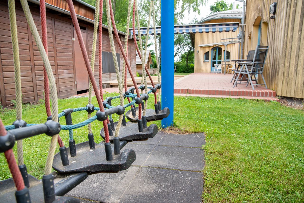 Kleine Schaukelsitze an einer Schaukel, im Hintergrund ein Schuppen und eine Terrasse mit Stühlen