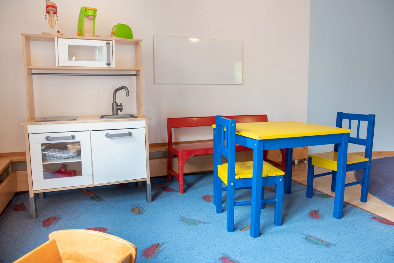 Spielecke einer Krippengruppe mit Spielküche, Sitzbank, Tisch und Stühlen auf einem Teppich