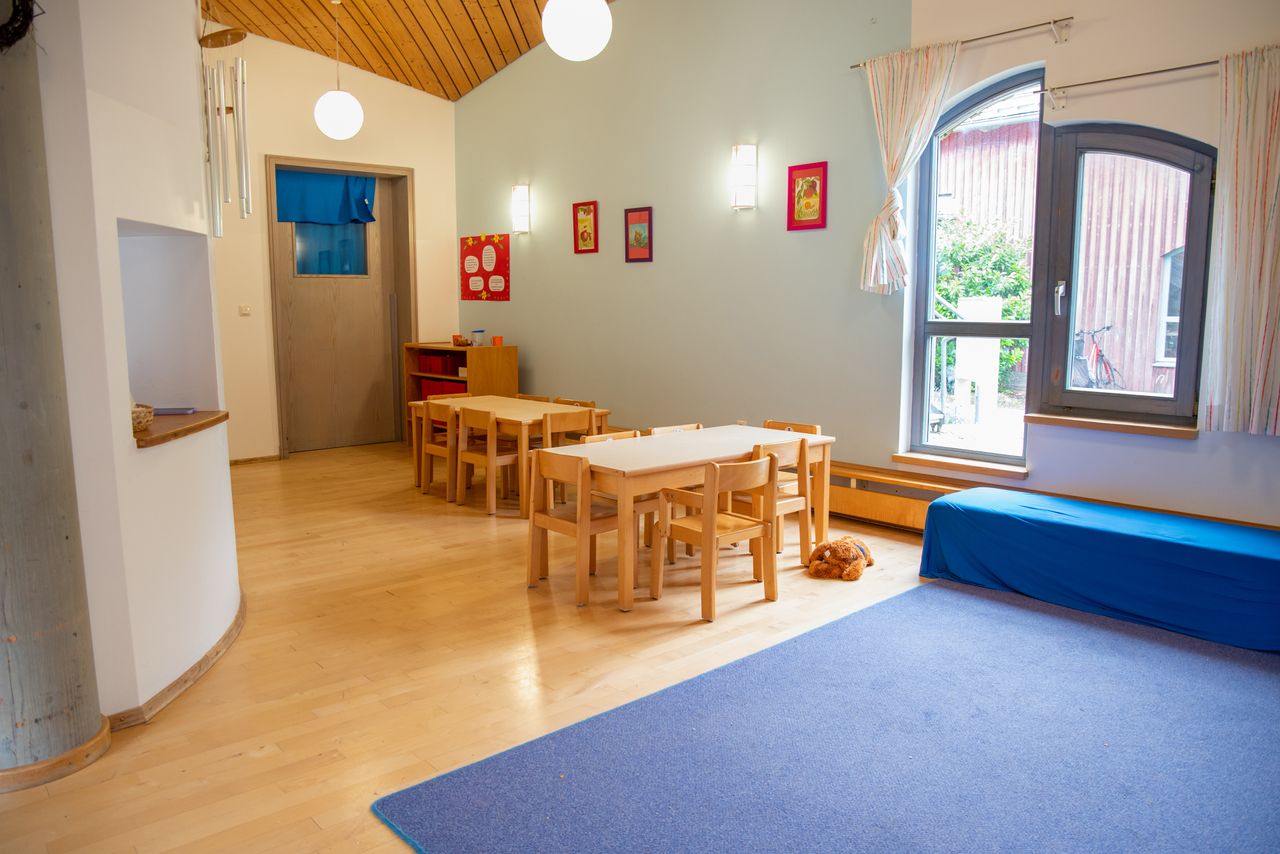 Ein Gruppenraum in der Kinderkrippe Unterm Regenbogen mit einer Kuschelecke, einem Teppich, Stühlen und Gruppentischen