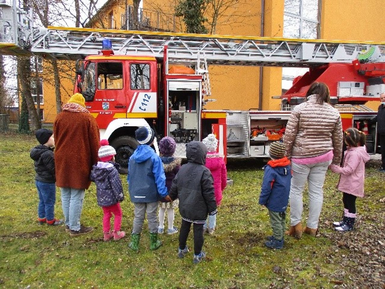 Eine Gruppe Kinder steht mit zwei Erwachsenen vor einer Drehleiter der Feuerwehr.
