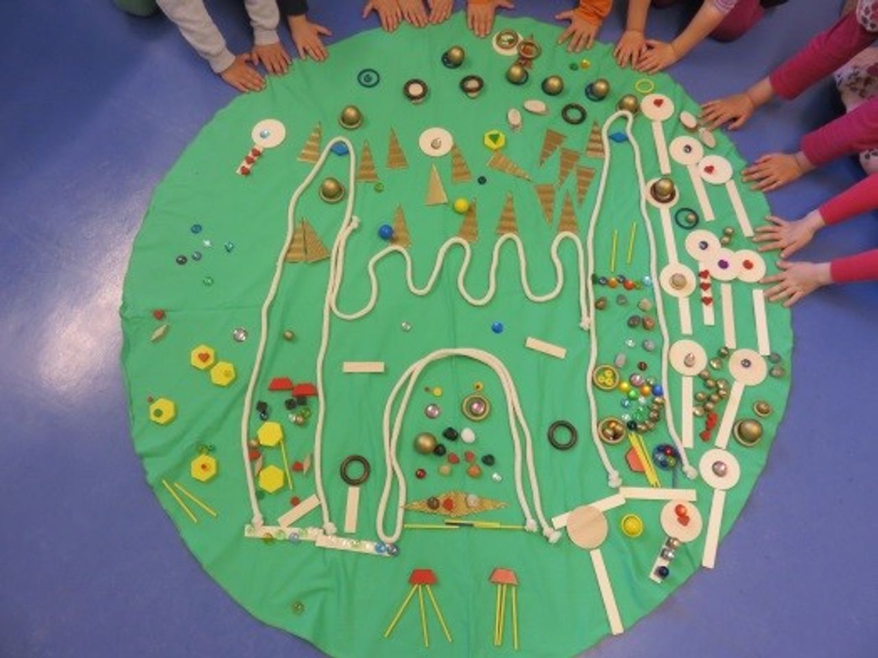 gelegtes Gemälde aus  grünem Kreisteppich mit kleinen Spielsachen