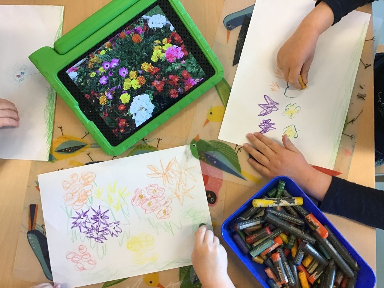 Kinder malen Bilder von Blumen, welche sie auf einem Tablet vor sich haben.