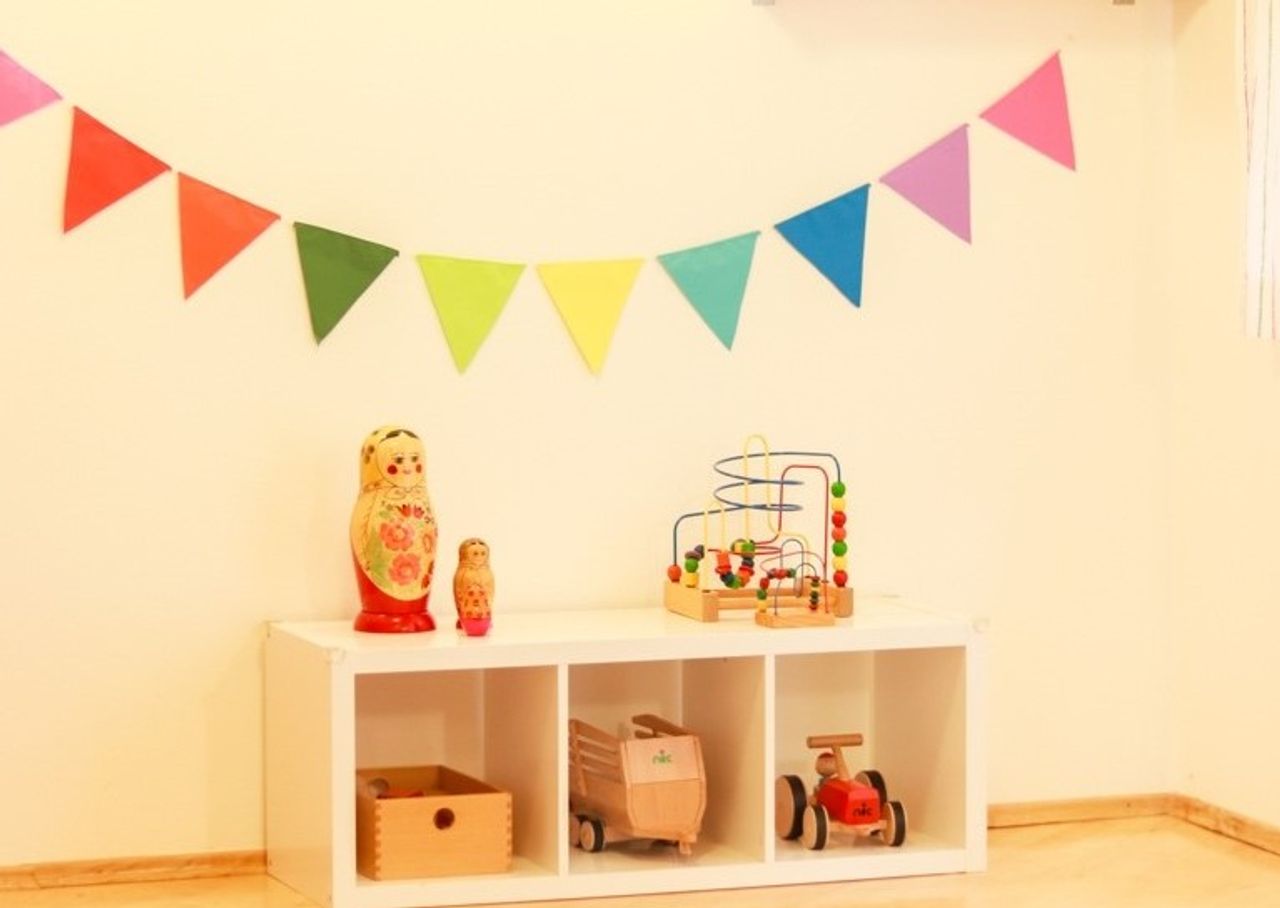 Eine Regenbogen-Girlande über einem kleinen Regal, in der Kinderkrippe "Unterm Regenbogen".