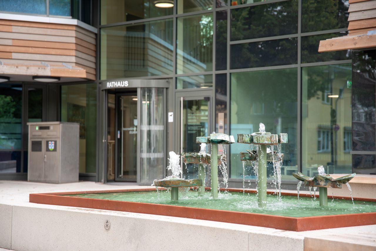 Außenansicht des Gröbenzeller Rathauses Außenansicht des Gröbenzeller Rathauses: im Vordergrund der sprudelnde Brunnen in Nahaufname, der Rathauseingang im Hintergrund leicht unscharf
