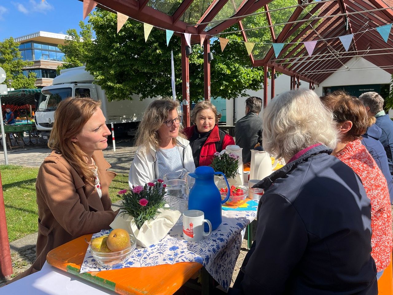 Damen und Herren sitzen an einem schön gedeckten Biertisch im der Sonne und unterhalten sich