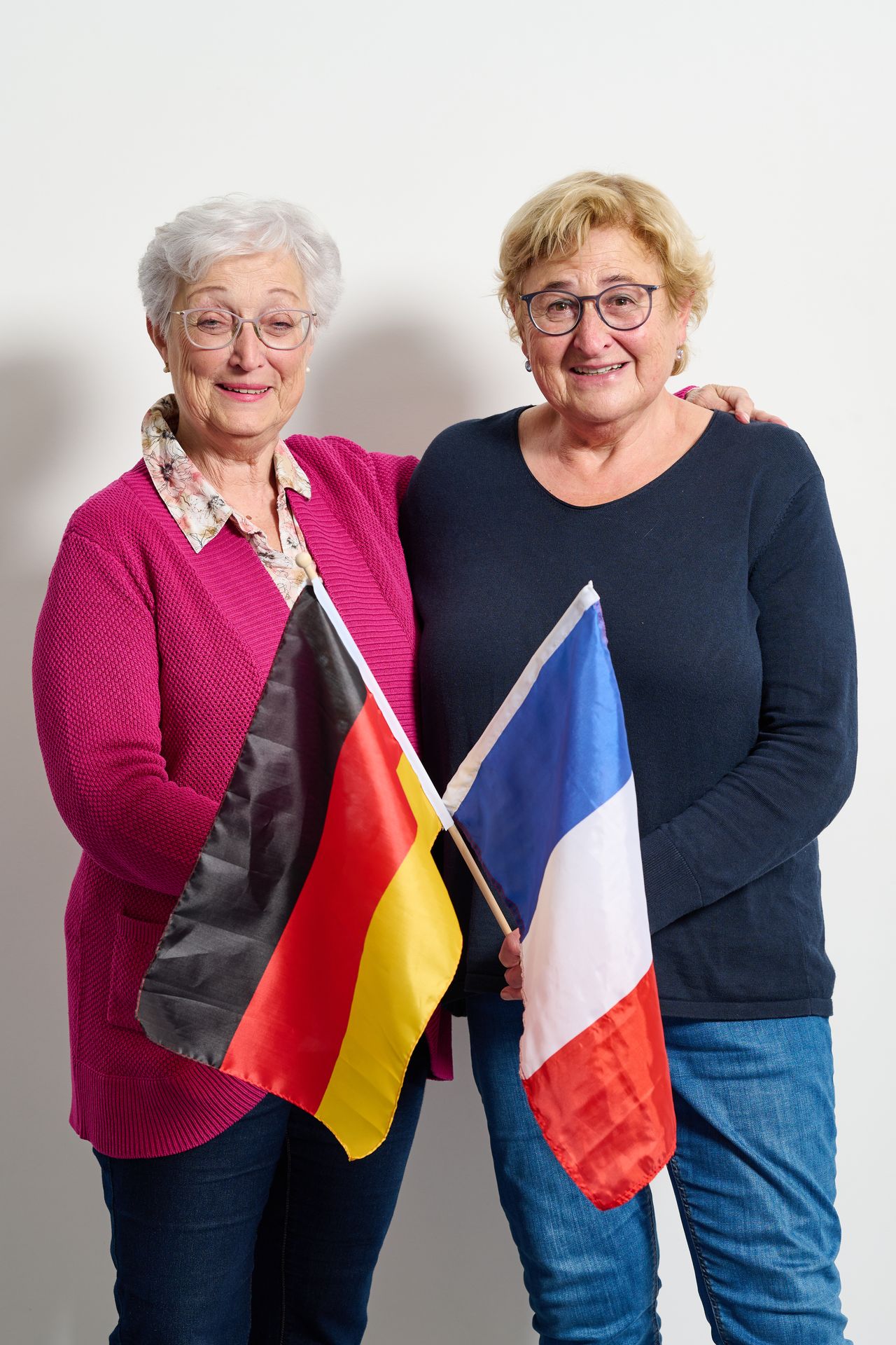 Zwei Frauen umarmen sich und haben eine Deutsche und eine Französische Flagge in der Hand.