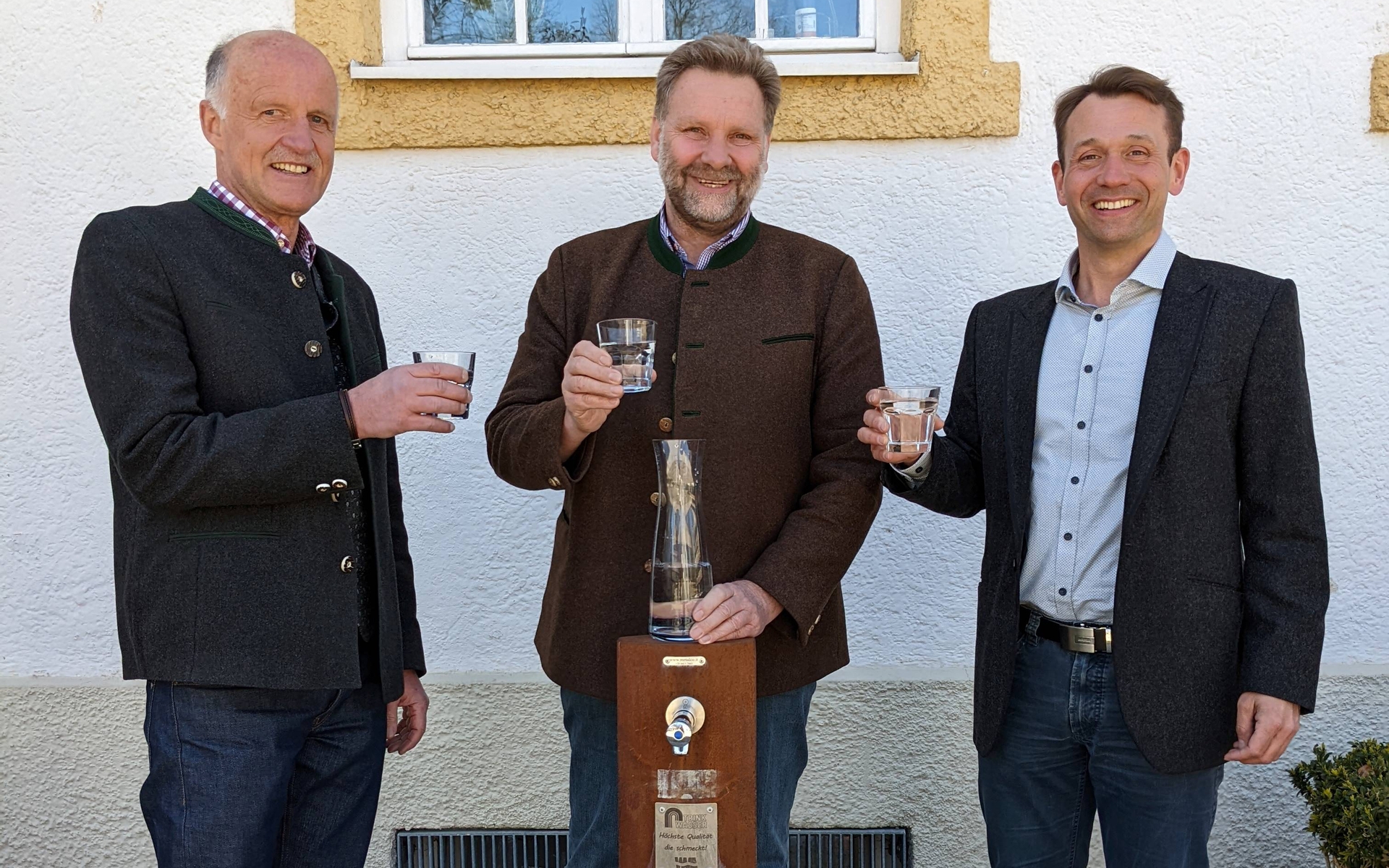 Erster Bürgermeister Martin Schäfer, Andreas Magg und Friedrich Popp stehen hinter dem Trinkwasserbrunnen mit einem Glas Wasser in der Hand