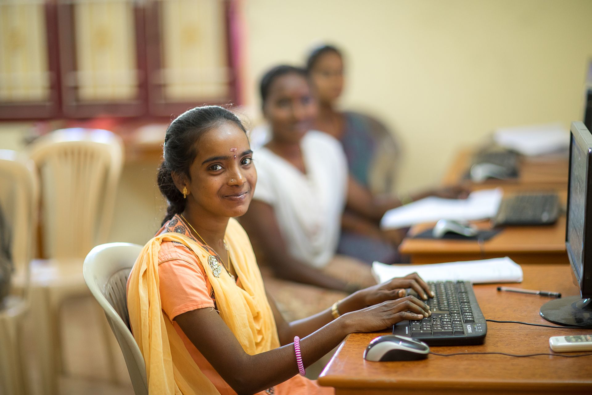Heartkids e.V. – ein Herz für die benachteiligten Mädchen Indiens Indisches Mädchen sitzt in einem Computer-Raum am PC. Im Hintergrund sind weitere Mädchen am PC zu sehen.