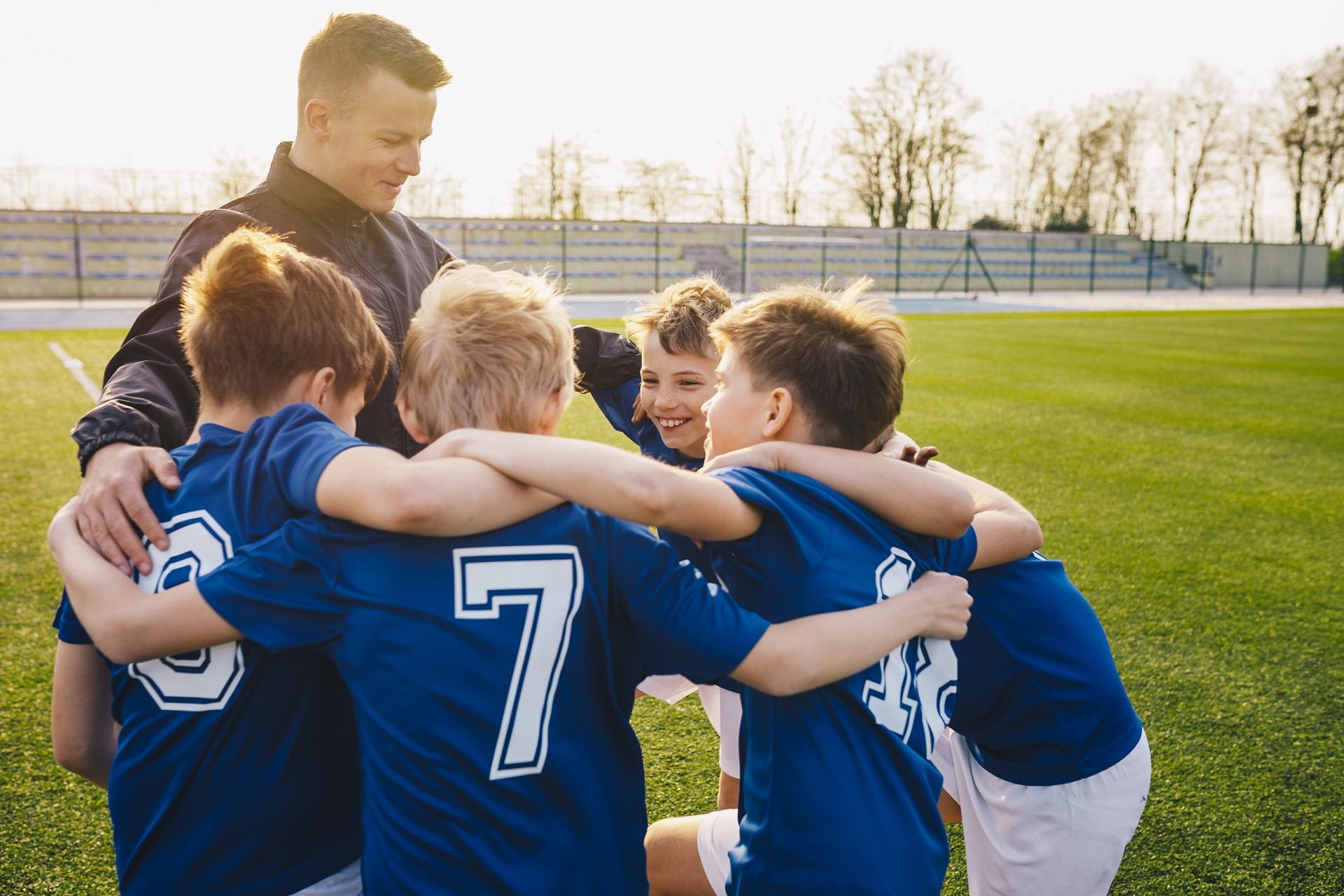 Auszeichnung Ehrenamt Trainer steht umgeben von Jungs im Fußballtrikot, die er trainiert, im Kreis. Alle umarmen sich