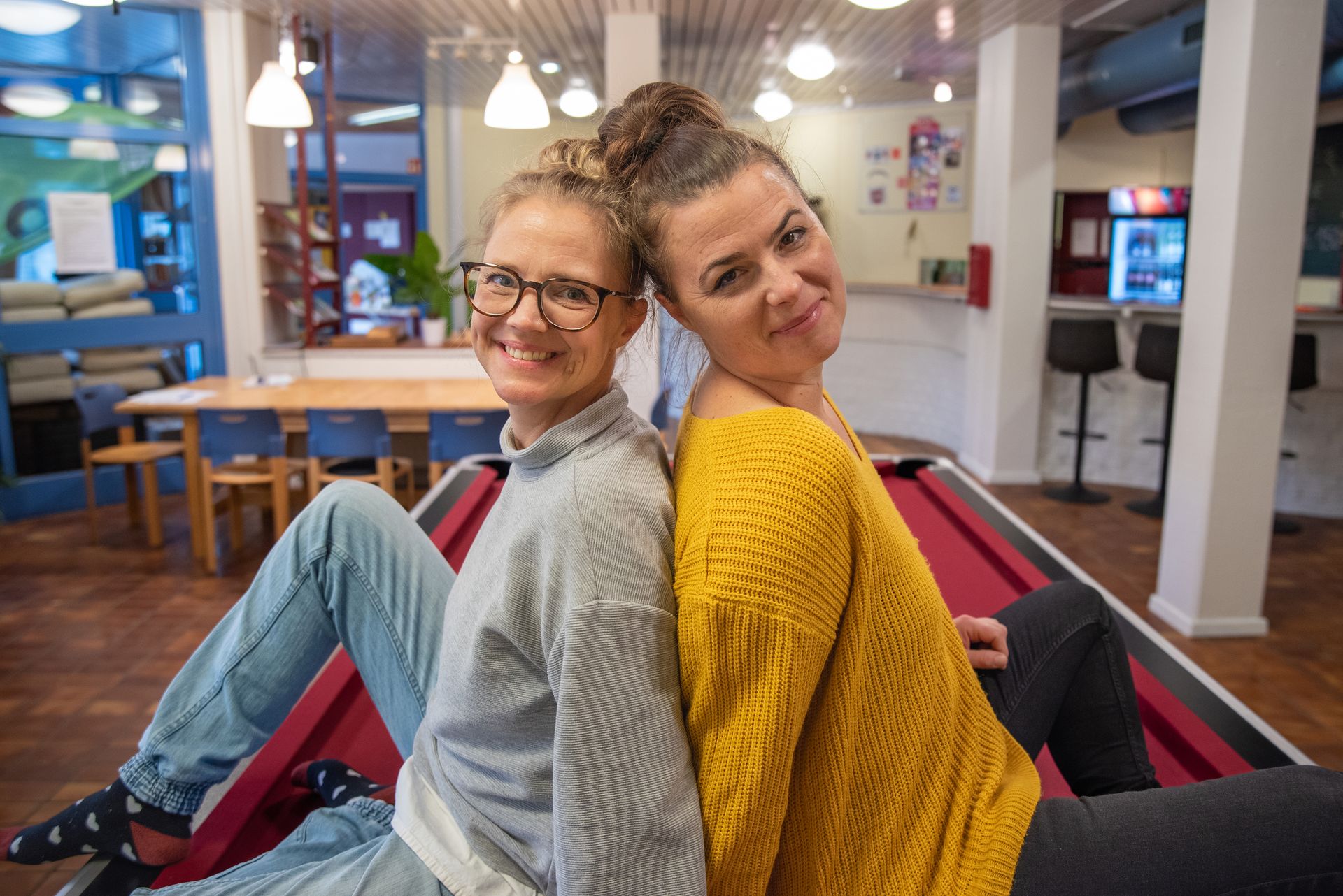 Steffi und Anna vom JBS-Team lehnen lächelnd Rücken an Rücken aneinander