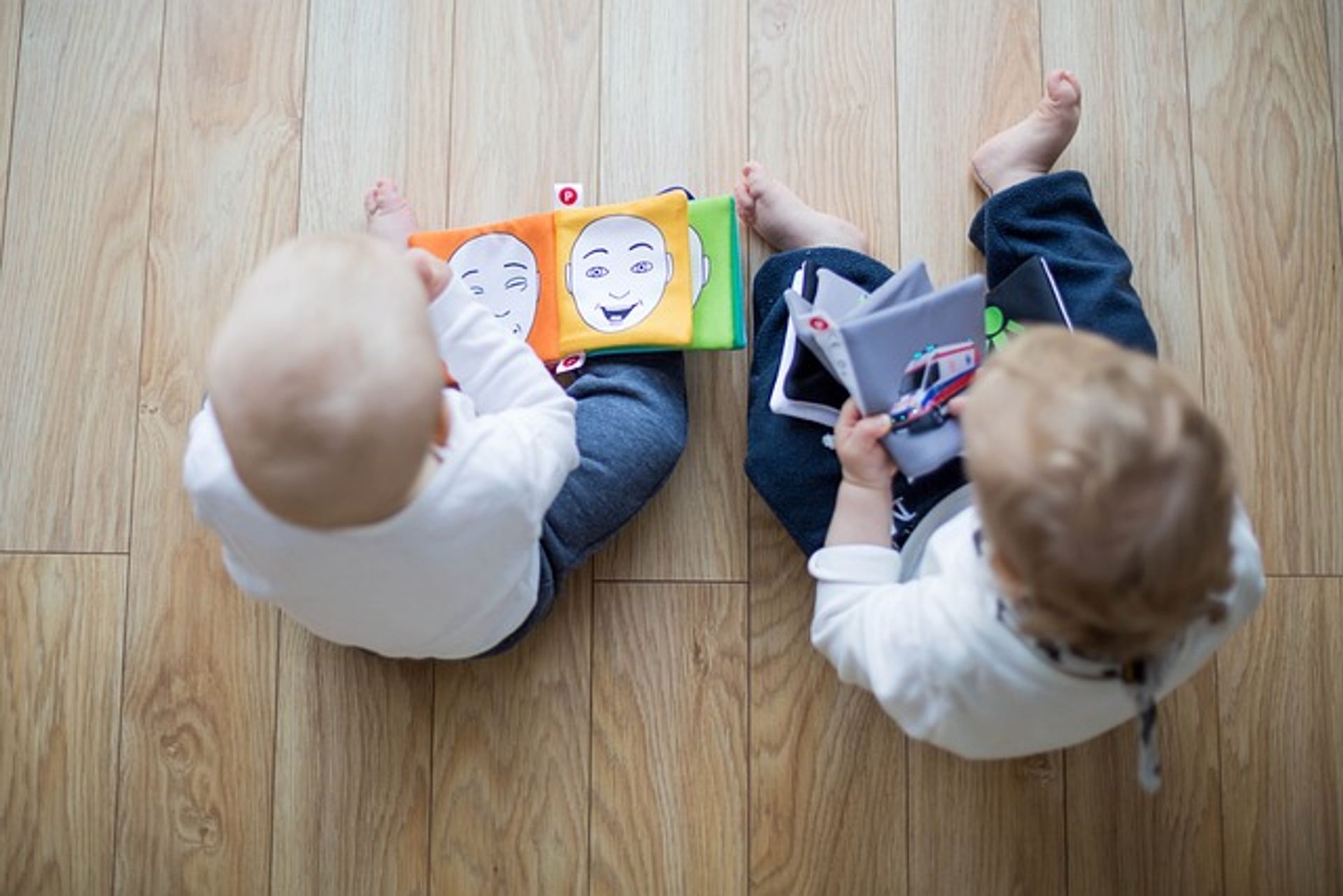 Bücher-Babys Zwei Kleinkinder sitzen mit dem rücken zum Betrachter auf dem Boden. Beide haben Erstlesebücher in der Hand.