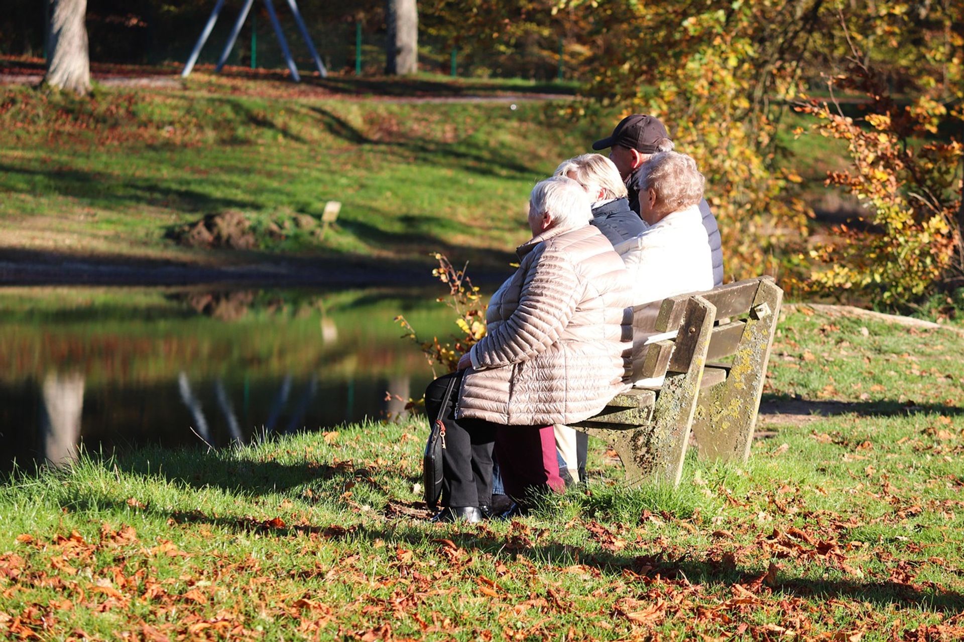 Nachbarschaft verbindet – Feierliche Eröffnung der Nachbarschaftsbank Herbststimmung und vier Personen sitzen nebeneinander auf einer Bank am Fluss