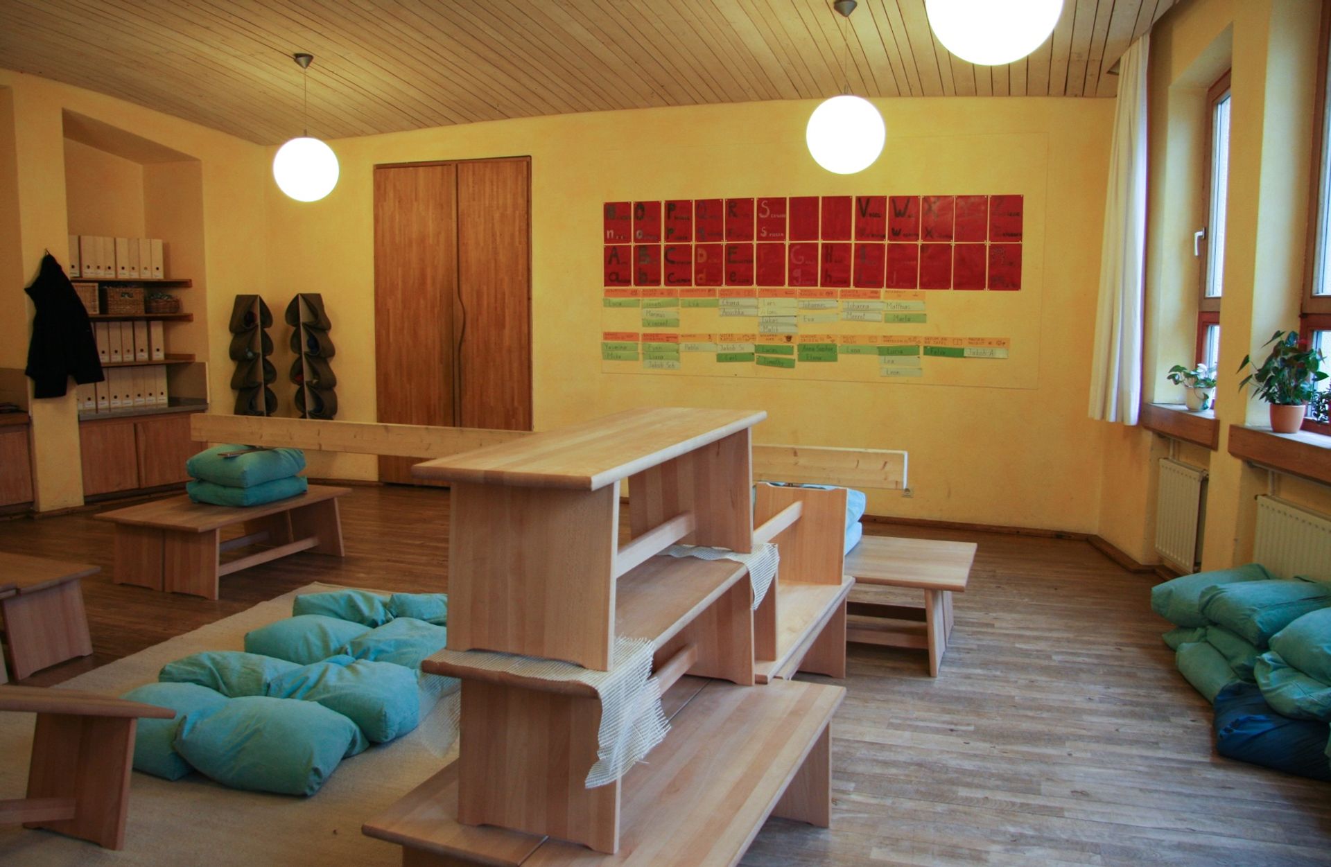 Foto eines Zimmers in der Schule mit Bänken, Kissen, Holz und warmen Farbtönen