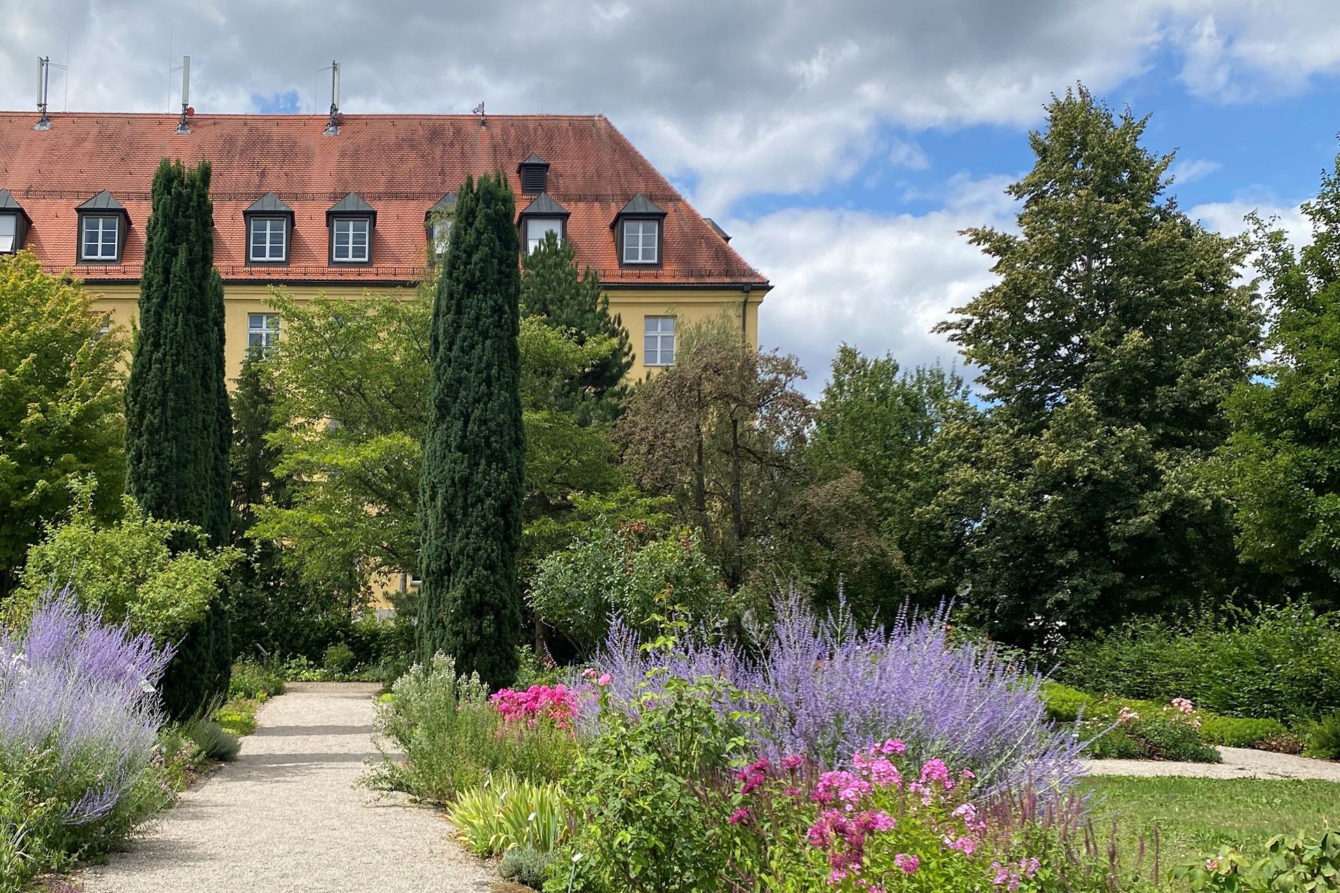 Foto eines blühenden Gartens. Im Hintergrund ein großes gelbes Haus.