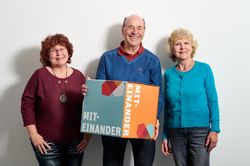 Drei Personen halten einen Würfel "Miteinander"
