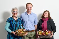 Drei Personen halten einen Korb voller Obst und Eingemachtem.