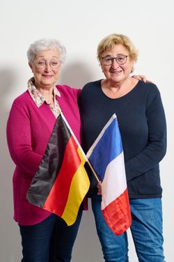 Zwei Frauen umarmen sich und haben eine Deutsche und eine Französische Flagge in der Hand.