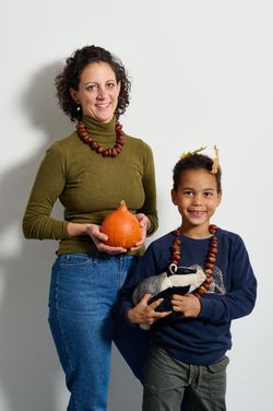 Frau steht mit Kürbis und Kind mit Kuscheltier Dachs und Blätter in den Haaren