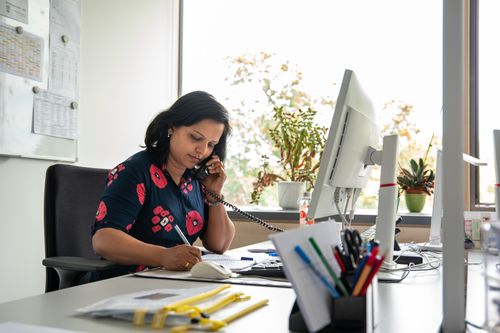  Mitarbeiterin sitzt am Schreibtisch, telefoniert und macht sich Notizen