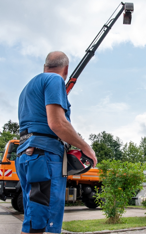  Mitarbeiter vom Gröbenzeller Betriebshof blickt mit umgeschnallter Kranfernbedienung auf den Kipper mit Teleskoparm