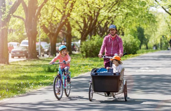 Vater fährt mit Lastenrad und zwei Kindern auf Fahrradweg