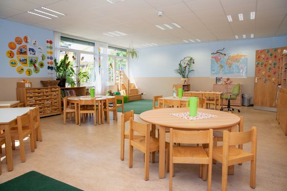 Gruppenraum im Kindergarten Wichtelhaus mit runden Gruppentischen und Stühlen rundherum sowie grünen Teppichen am Boden