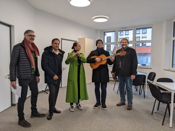 Der Architekt des Gebäudes, Vertreter und Vertreterin der Musikschule und der Bürgermeister stehen in den neuen Räumen und testen die Klang mit Musikinstrumenten.