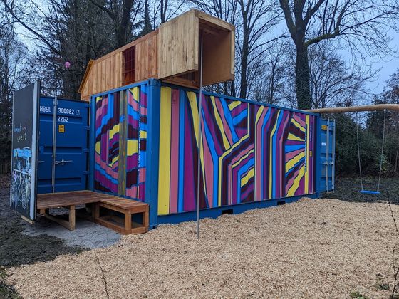 Spielcontainer Außenansicht des Spielcontainers von der Rückseite: Bunt bemalter Schiffscontainer mit Holzaufbau, Rutschstange und integrierter Schaukel