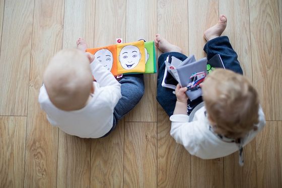 Bücher-Babys Zwei Kleinkinder sitzen mit dem rücken zum Betrachter auf dem Boden. Beide haben Erstlesebücher in der Hand.