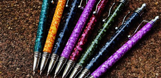 Mehrere bunte Kugelschreiber auf einem Untergrund aus Kies